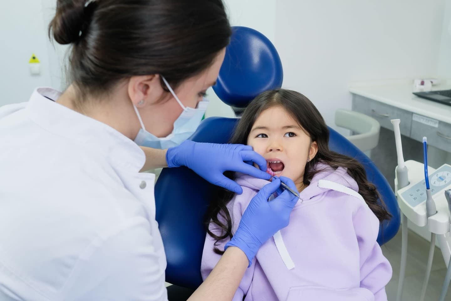 A female dentist gently examining a young girl's teeth in a bright clinical setting