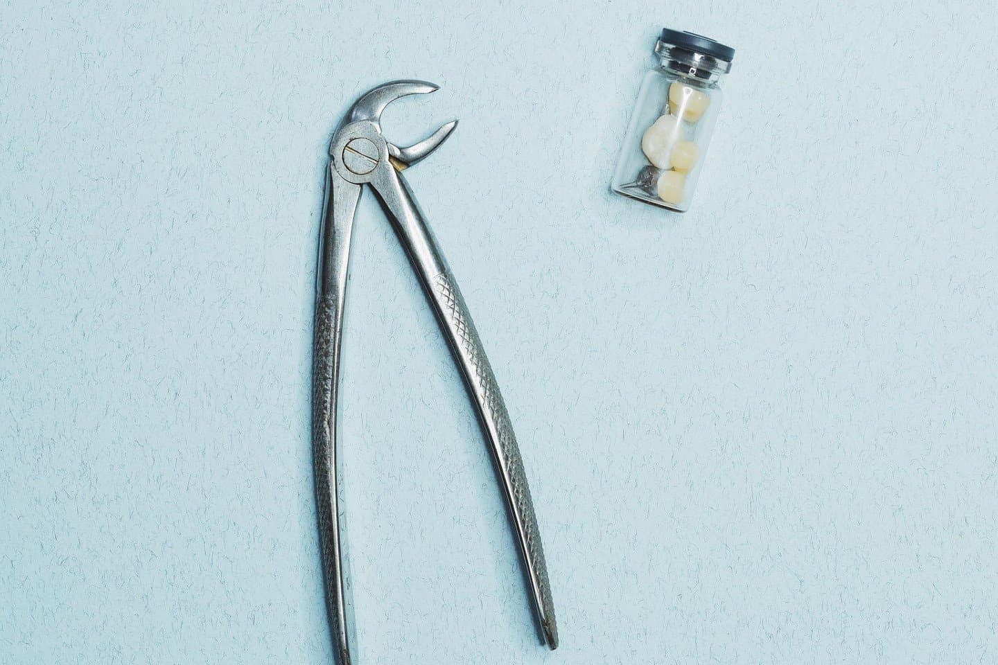 A tooth extraction forceps next to a small vial holding an extracted tooth