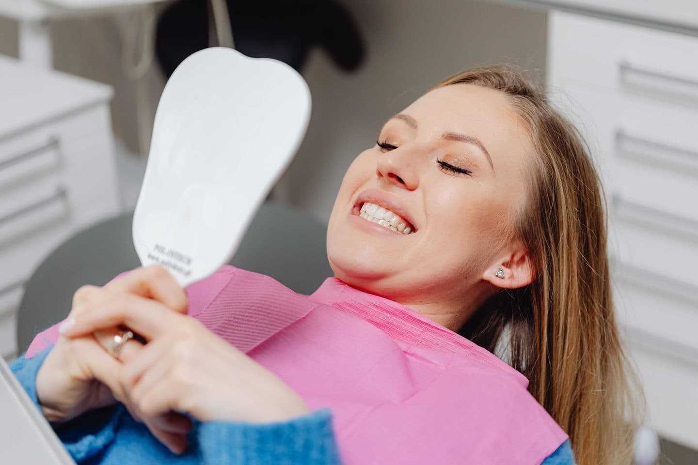 A woman in a dental chair looking at her smile in a mirror