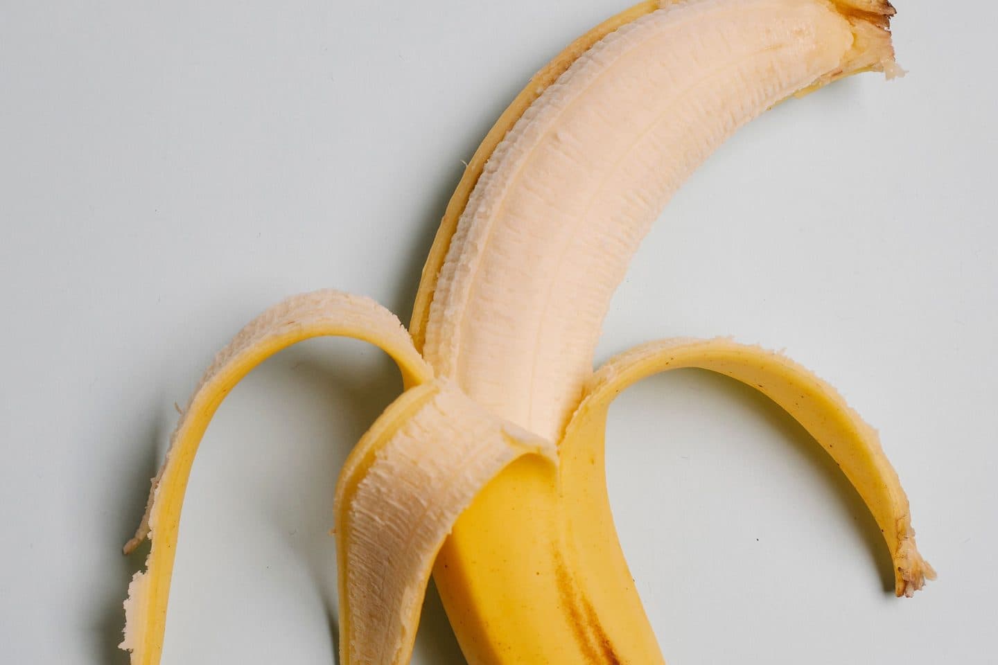 A banana with its peel half pulled back, resting on a light-colored surface