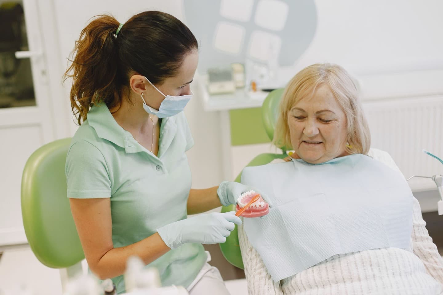 A dentist showing a denture model to an elderly patient in a consultation room