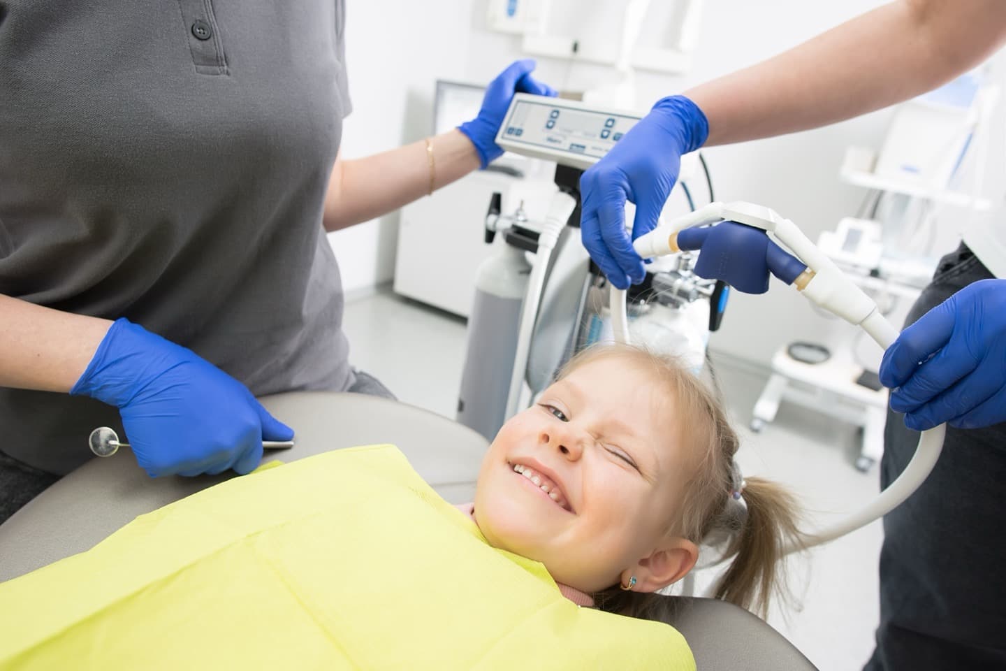 A smiling child in a dental chair being examined by a dental team
